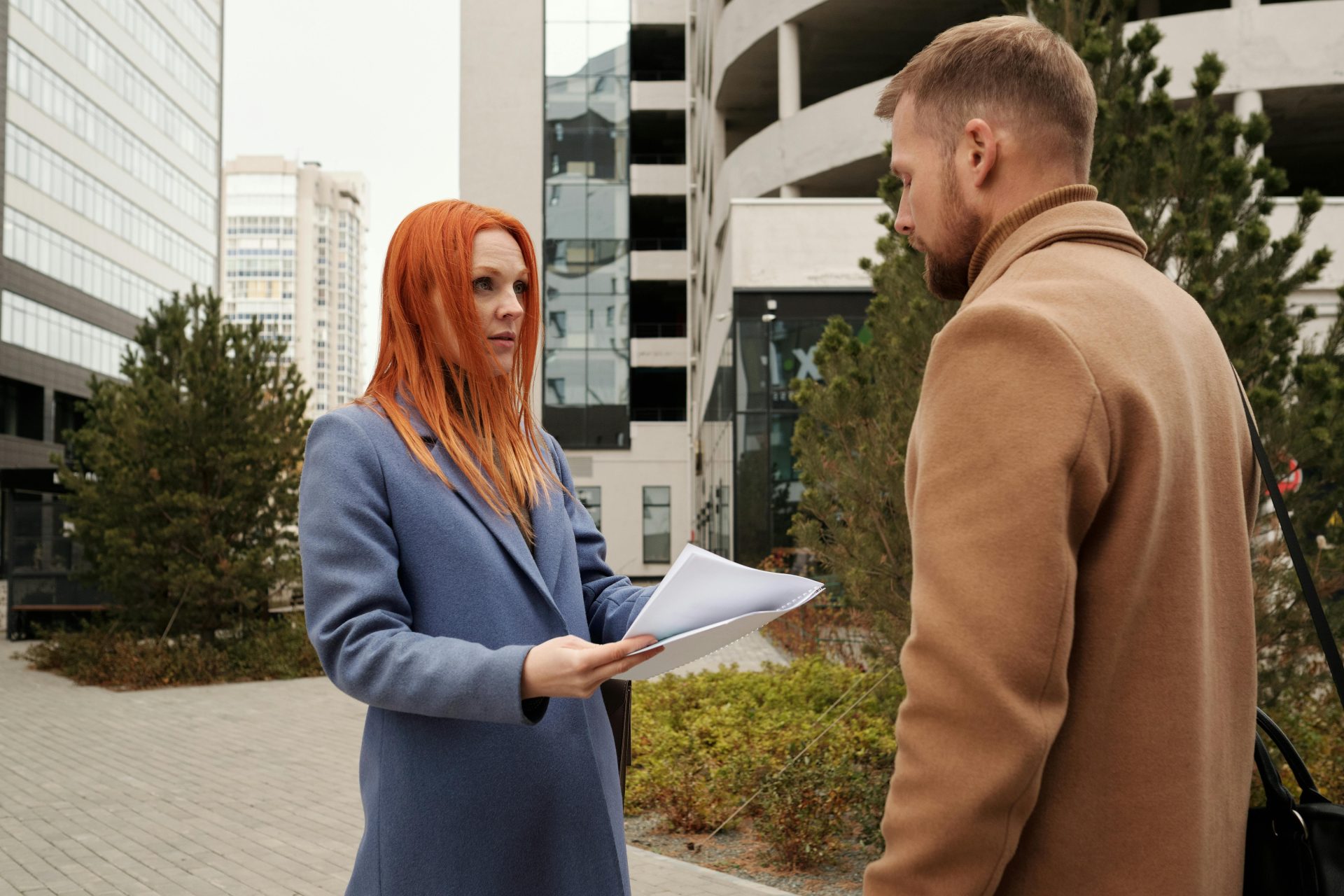 Man and woman in corporate attire engaging in conversation outside urban office complex.